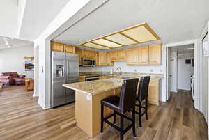 Kitchen with stainless steel appliances, a kitchen island, light stone countertops, light wood-type flooring, and light brown cabinets