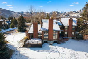 Snow covered rear of property featuring a chimney and a deck with mountain view