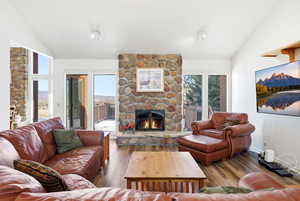 Living room with lofted ceiling, a stone fireplace, wood-type flooring, and healthy amount of natural light