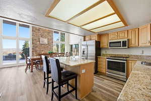 Kitchen with appliances with stainless steel finishes, a kitchen island, light wood-style floors, light stone countertops, and a textured ceiling