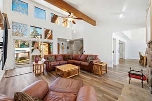 Living room featuring beamed ceiling, a ceiling fan, wood finished floors, stairs, and high vaulted ceiling