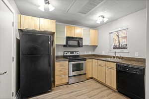 Kitchen with light brown cabinetry, black appliances, dark countertops, light wood-type flooring, and a textured ceiling