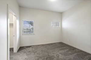Unfurnished bedroom featuring a walk in closet, carpet flooring, and multiple windows