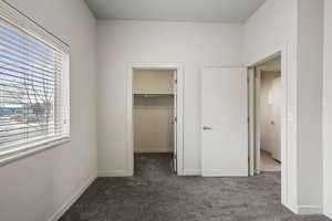 Unfurnished bedroom featuring dark carpet and a walk in closet