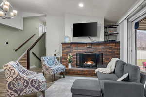 Living room with lofted ceiling, stairway, a brick fireplace, wood finished floors, and a chandelier