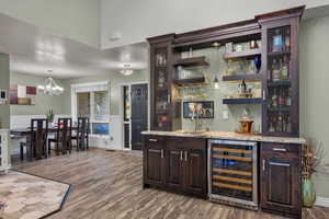 Indoor wet bar featuring dark brown cabinetry, wine cooler, dark wood finished floors, open shelves, and light stone counters