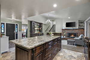 Kitchen featuring dark brown cabinetry, a brick fireplace, black range with gas stovetop, light stone counters, and vaulted ceiling