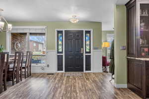 Foyer entrance with plenty of natural light, wood finished floors, a chandelier, and a wainscoted wall
