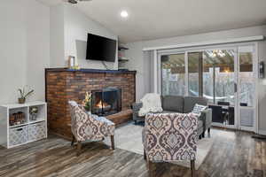 Living area featuring vaulted ceiling, wood finished floors, a brick fireplace, and recessed lighting