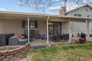 Back of property with a chimney, a patio area, a hot tub, and a lawn
