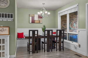 Dining area with dark wood-type flooring, a chandelier, and a wainscoted wall
