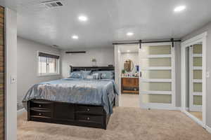 Carpeted bedroom with a barn door, ensuite bathroom, and recessed lighting
