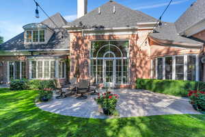Rear view of property featuring brick siding, a patio, a chimney, roof with shingles, and a lawn