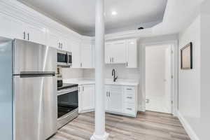 Kitchen featuring stainless steel appliances, white cabinets, light wood-style flooring, and light stone counters