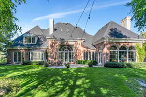 Rear view of house featuring a chimney, brick siding, a patio, and a lawn