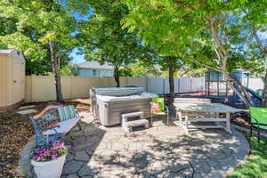 Fenced backyard featuring a patio, a hot tub, a playground, and a storage unit