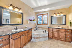 Full primary suite bathroom with two vanities, a garden tub, and light tile patterned floors