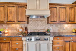 Kitchen with dark stone countertops, brown cabinetry, stainless steel gas stovetop, and range hood