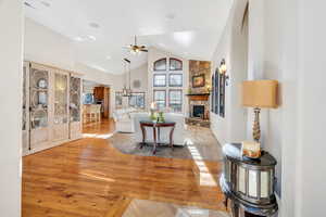 Living room with high vaulted ceiling, wood floors, ceiling fan, and a fireplace