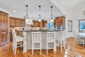 Kitchen with a kitchen bar, brown cabinetry, hanging light fixtures, dark stone counters, and recessed lighting