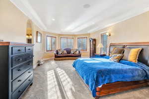 Primary suite featuring crown molding, light colored carpet, arched walkways, and recessed lighting