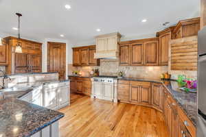 Kitchen with dark stone counters, brown cabinetry, pendant lighting, light wood-style flooring, and recessed lighting
