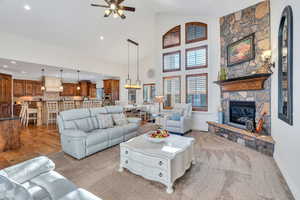 Living area featuring high vaulted ceiling, a fireplace, a ceiling fan, and light carpet