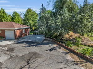 View of side of property with brick siding, driveway, a garage, and roof with shingles