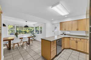 Kitchen featuring a peninsula, dishwasher, pendant lighting, light brown cabinetry, and light tile patterned floors