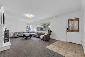 Living area featuring a brick fireplace, light colored carpet, crown molding, and light tile patterned floors