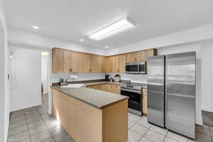Kitchen with appliances with stainless steel finishes, recessed lighting, a peninsula, light tile patterned floors, and light brown cabinets