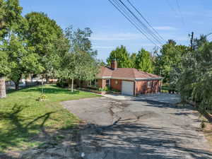 View of front of property with driveway, a front yard, an attached garage, a chimney, and brick siding