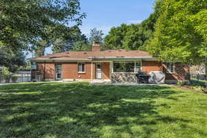 Back of property featuring brick siding, a patio area, a chimney, and a shingled roof