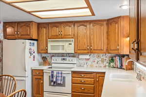 Kitchen featuring white appliances, brown cabinets, light countertops, and a textured ceiling