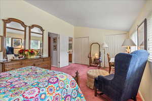 Carpeted bedroom featuring vaulted ceiling and multiple closets