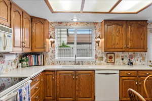 Kitchen with white appliances, a sink, wallpapered walls, brown cabinetry, and light countertops