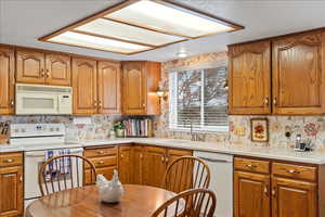 Kitchen featuring white appliances, brown cabinetry, and decorative backsplash