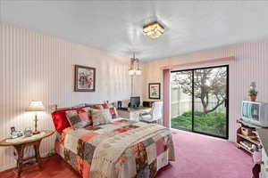 Bedroom with carpet floors, a textured ceiling, access to exterior, a desk, and wallpapered walls