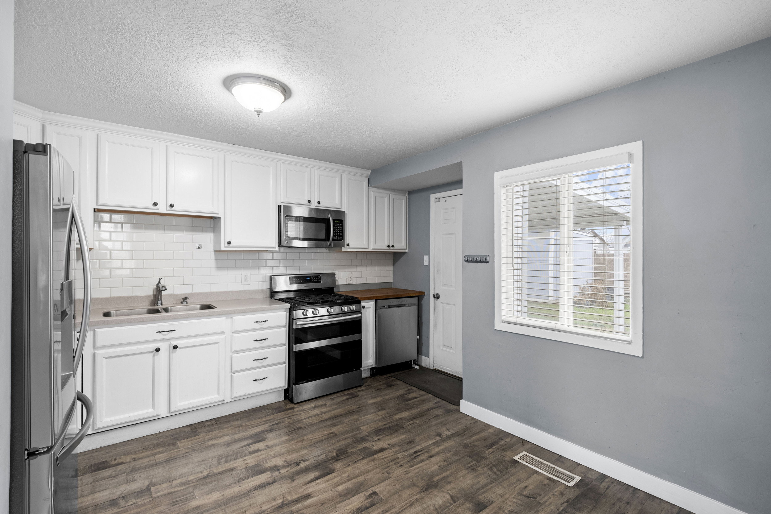Kitchen featuring appliances with stainless steel finishes, white cabinets, a textured ceiling, tasteful backsplash, and light countertops