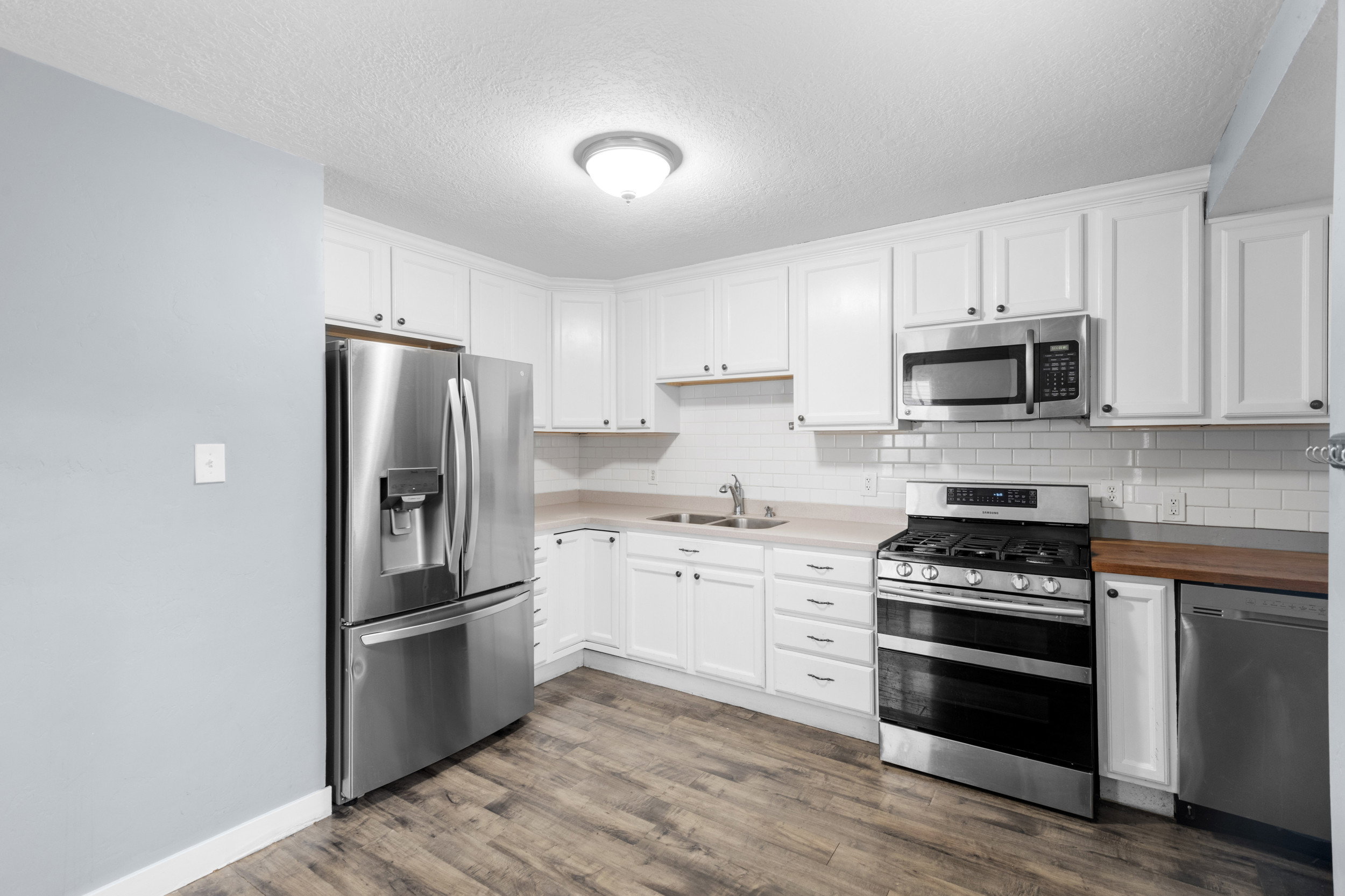 Kitchen featuring appliances with stainless steel finishes, white cabinets, a textured ceiling, dark wood finished floors, and tasteful backsplash