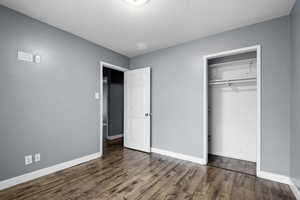 Unfurnished bedroom with a textured ceiling, a closet, and dark wood-style floors