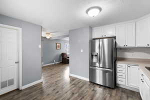 Kitchen with white cabinets, stainless steel refrigerator with ice dispenser, a textured ceiling, ceiling fan, and dark wood-style flooring