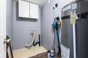 Laundry area featuring water heater, tile patterned floors, cabinet space, and washer hookup