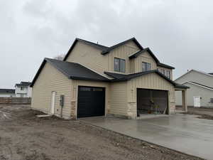 View of property exterior with board and batten siding, concrete driveway, stone siding, and a shingled roof