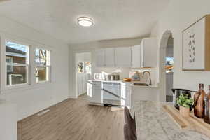 Kitchen with white cabinets, stainless steel dishwasher, light wood-style floors, light stone counters, and a textured ceiling