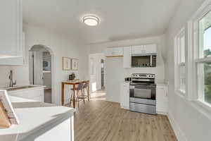 Kitchen featuring stainless steel appliances, arched walkways, light countertops, white cabinetry, and light wood-style floors
