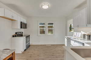 Kitchen with stainless steel appliances, white cabinetry, and light wood-style flooring