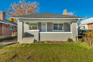 Bungalow-style house featuring a porch, a front lawn, a chimney, and stucco siding