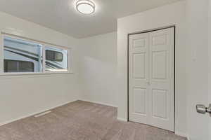 Unfurnished bedroom featuring light carpet, a closet, and a textured ceiling