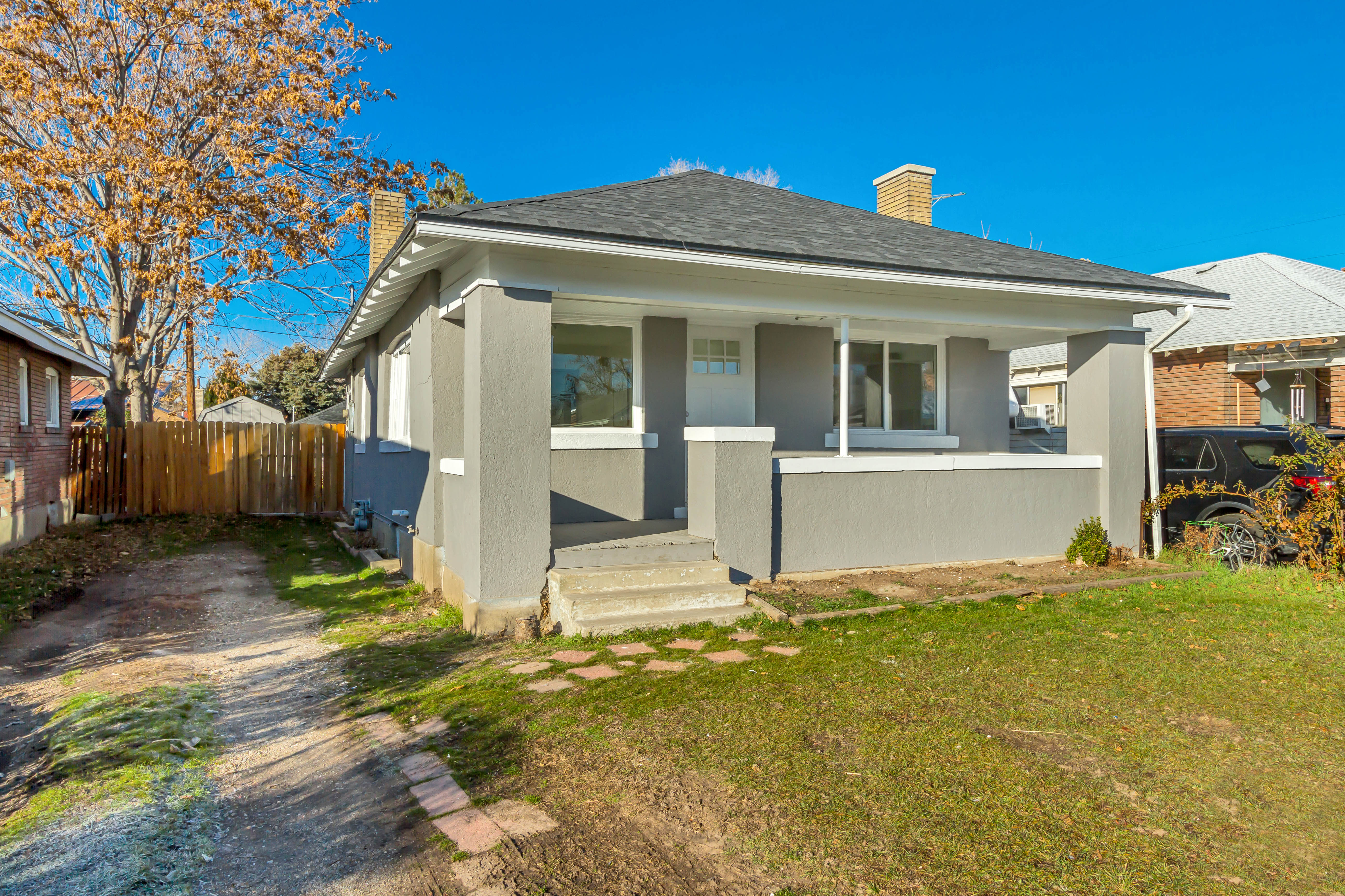 View of front of house with a chimney, covered porch, stucco siding, and a shingled roof